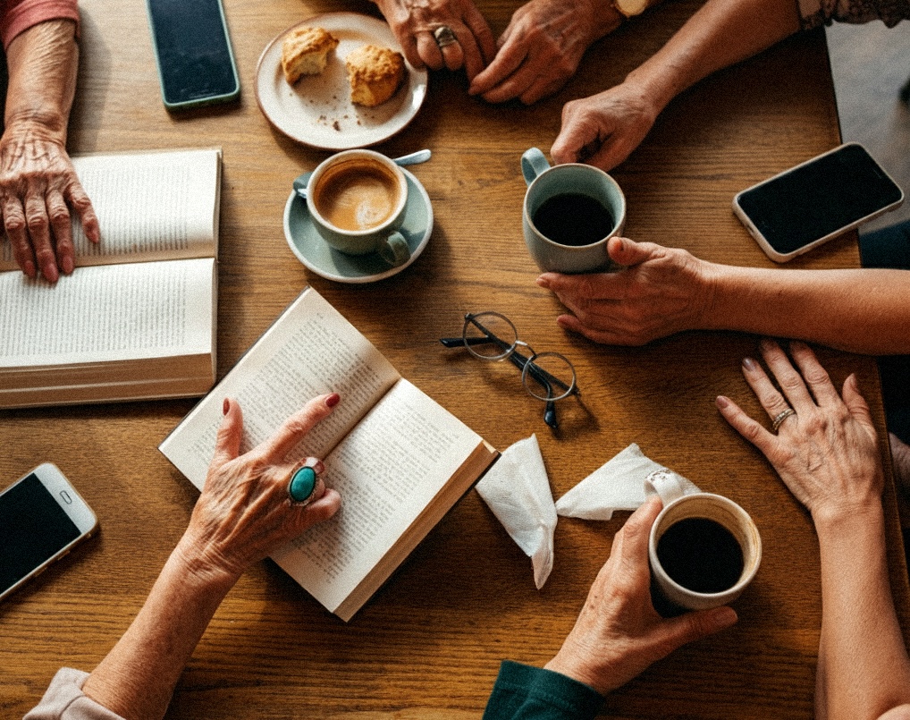 Senior women's hands around coffee shop table with phones and books, illustrating active social lifestyle benefits of rightsized community living